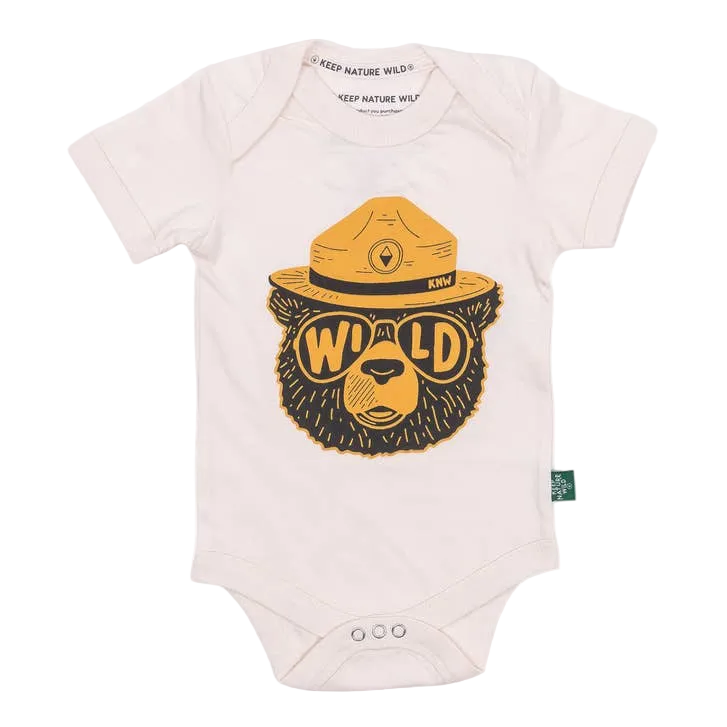 A white short-sleeve baby bodysuit featuring a large graphic of a bear wearing a yellow ranger hat and yellow sunglasses with the word 'WILD' across the eyes. The brand 'Keep Nature Wild' is visible on the inner neck label and as a small green tag on the side.