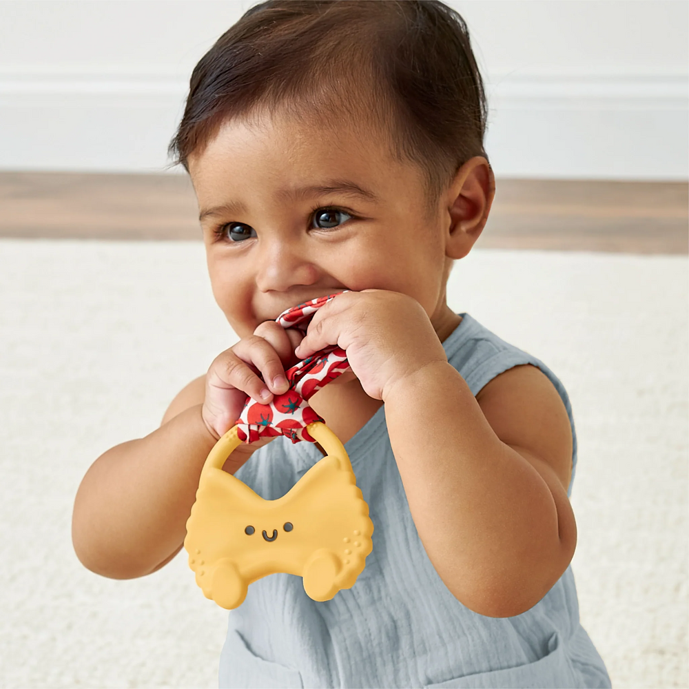 Baby holding a yellow teething toy with a red and white patterned ribbon.