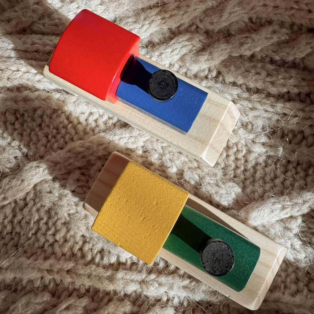 Two wooden sliding block toys with colorful rectangular panels and black circular weights, placed on a beige chunky knit blanket.