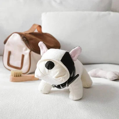 Plush toy bulldog on a light-colored surface with a bag and toothbrush in the background
