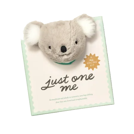 A koala plush toy attached to a book titled "just one me" in a baby gift set. The plush is light gray with white ears and a small green collar.