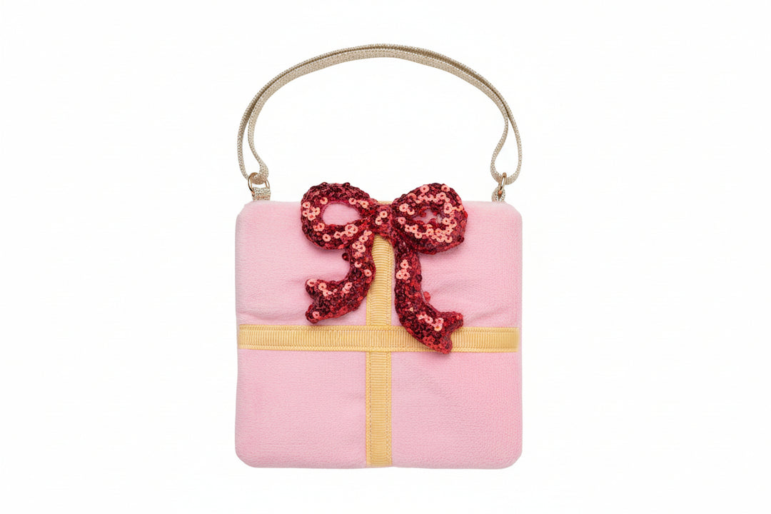 A pink gift box purse with a gold strap, featuring a yellow ribbon graphic and a red sequined bow on the front.